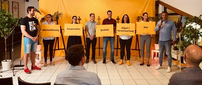 Das Management von JobRouter steht auf einer Bühne. Sie halten je eine Tafel in der Hand auf welcher einer der JobRouter-Werte abgedruckt ist. 